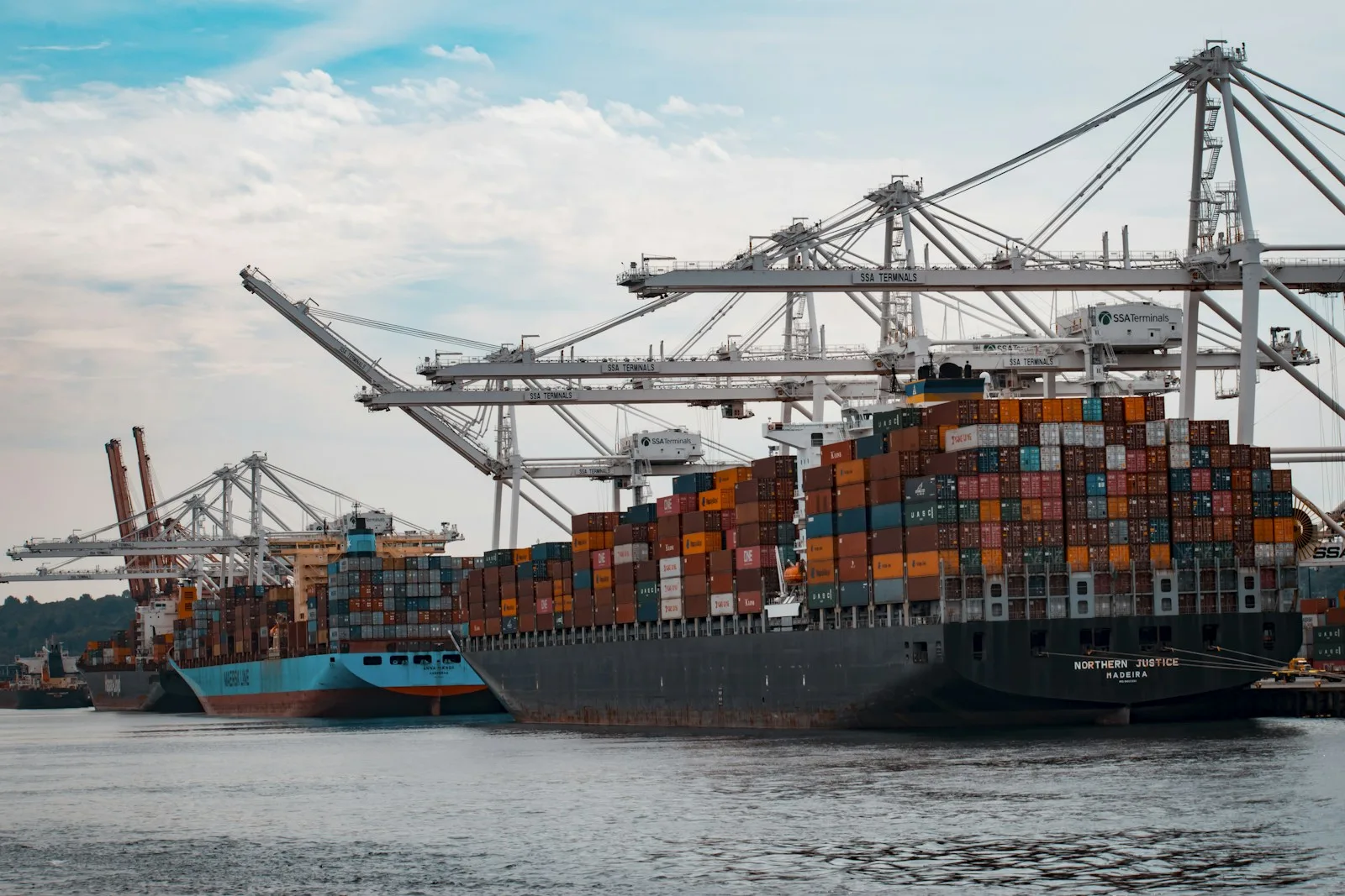 Portacontenedores atracado con grúas de pórtico: elegir el incoterm define quién paga hasta este punto y desde dónde sigue el comprador